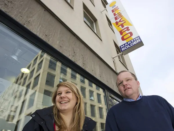 Zwei Mitarbeitende vor dem Firmenschild in der Alten Wallgasse